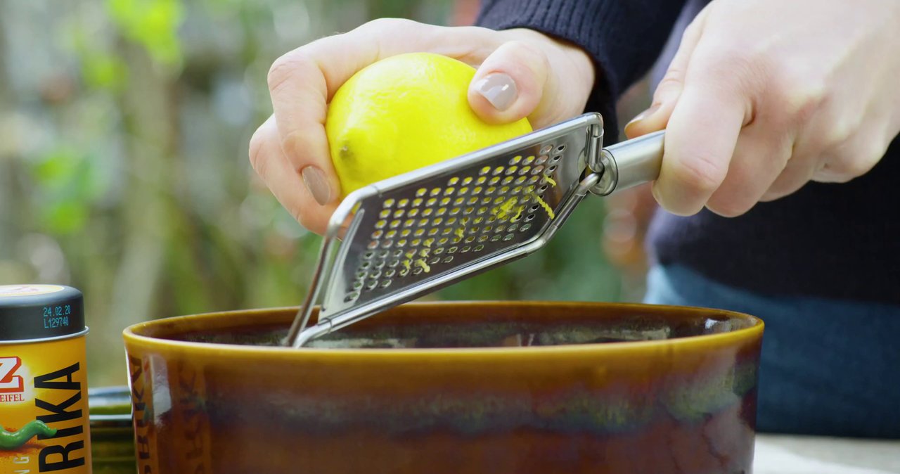 Hands zesting a fresh lemon into a ceramic bowl